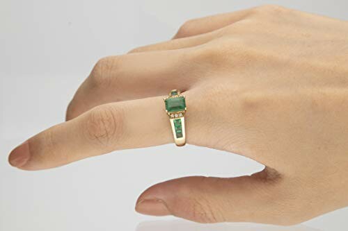 Hand wearing a gold ring with a green emerald stone