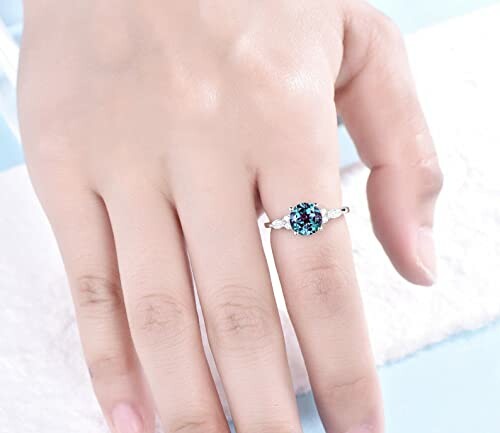 Hand wearing a silver ring with a blue gemstone.